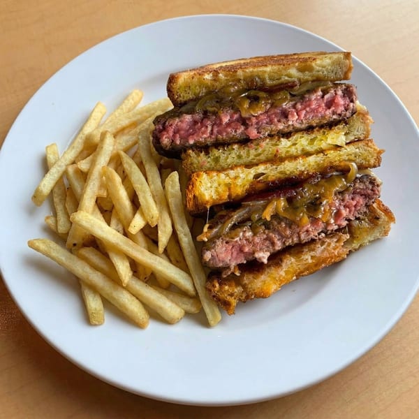 A grilled cheese burger, cut in half, revealing a medium-rare patty and caramelized onions, served with fries.