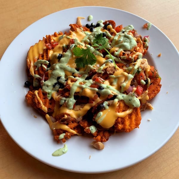Sweet potato waffle fries topped with cheese sauce, black beans, salsa, and green crema.