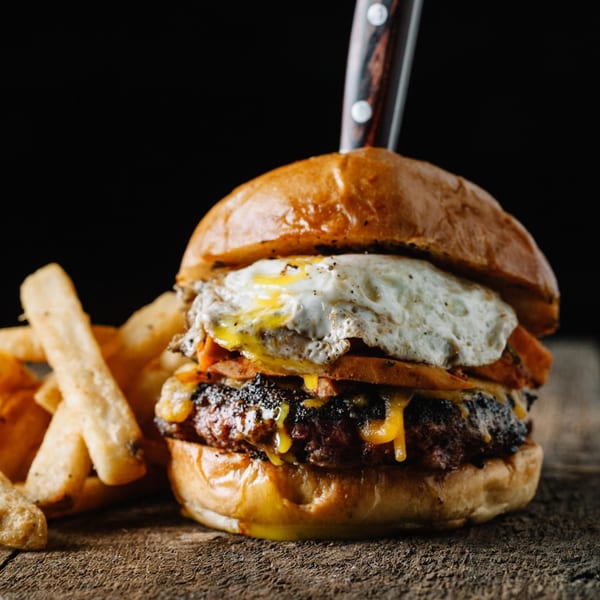 Gourmet burger with a fried egg, melted cheese, and fries on a rustic wooden surface.