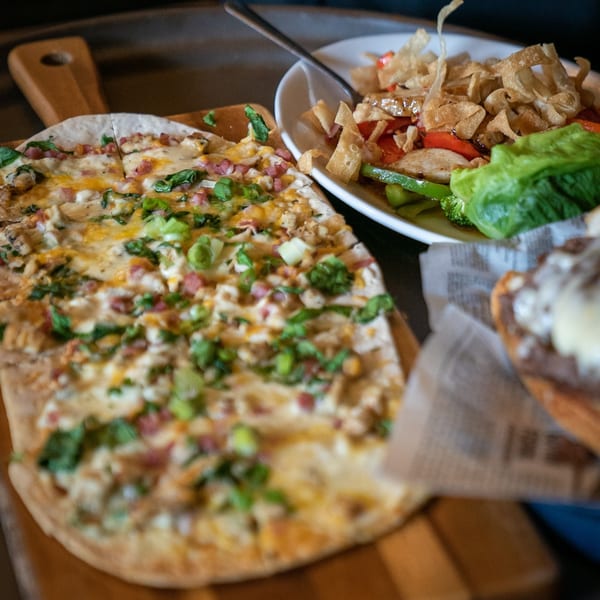 Flatbread pizza with cheese, bacon, and green onions, next to a salad with crispy wontons.