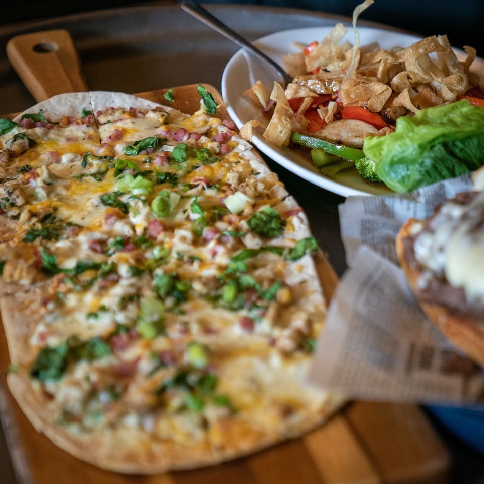 Flatbread pizza with cheese, bacon, and green onions, next to a salad with crispy wontons.