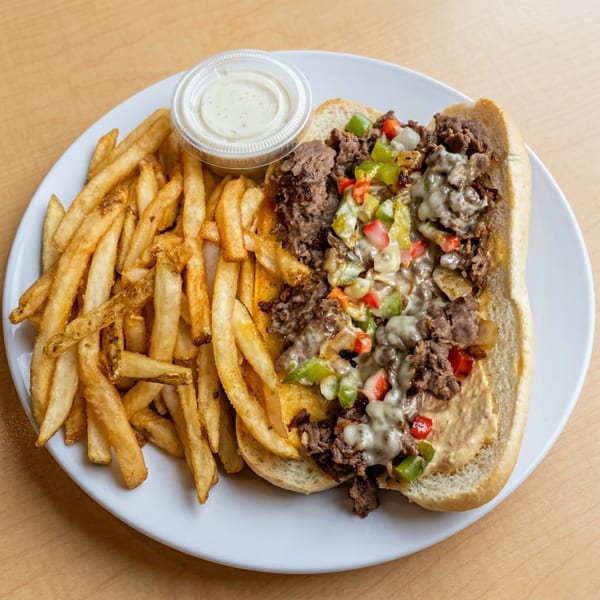 Cheesesteak sandwich with peppers, onions, and melted cheese, served with a side of fries and dipping sauce.