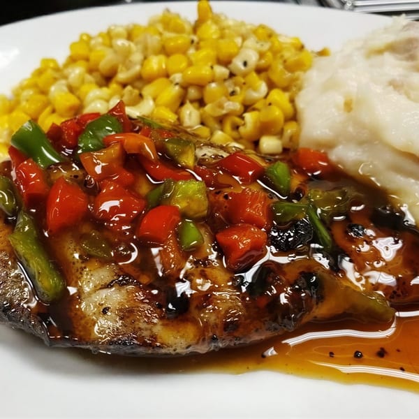 Grilled fish topped with colorful bell peppers and sauce, served with corn and mashed potatoes.