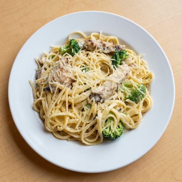 Creamy chicken and broccoli pasta with grated cheese on a white plate.
