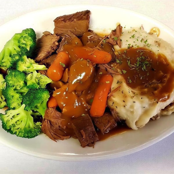 A plate of pot roast with gravy, carrots, mashed potatoes, and steamed broccoli.
