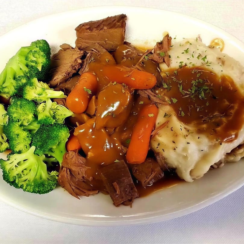 A plate of pot roast with gravy, carrots, mashed potatoes, and steamed broccoli.