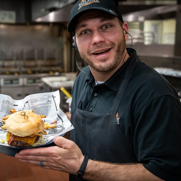 A smiling Badlands Restaurant & Bar employee holds a burger and fries in a kitchen.