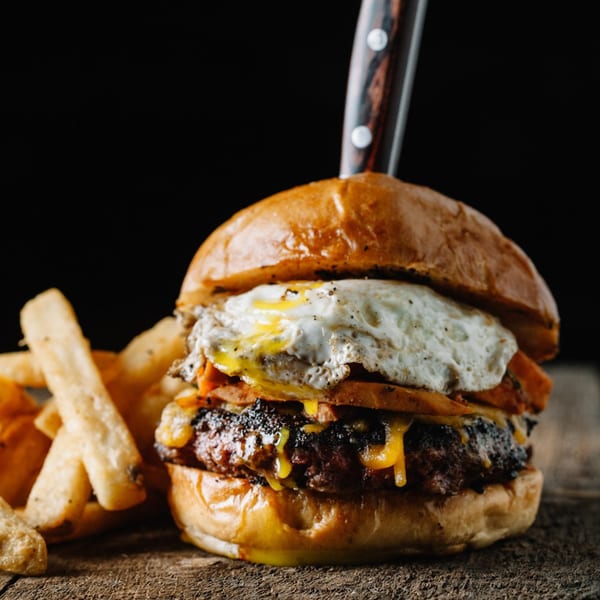 Gourmet burger with a fried egg, bacon, and melted cheese, served with fries.